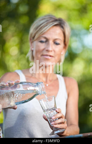Cute femme versant de l'eau dans un verre dans son jardin en plein air Banque D'Images