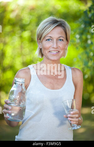 Cute femme versant de l'eau dans un verre dans son jardin en plein air Banque D'Images