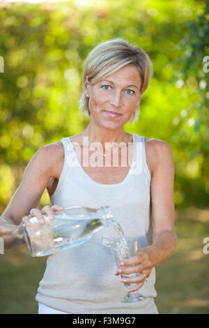 Cute femme versant de l'eau dans un verre dans son jardin en plein air Banque D'Images