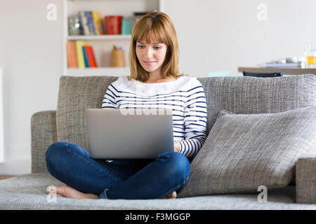 Mid adult woman sur son canapé à l'aide d'ordinateur portable à la maison. Banque D'Images