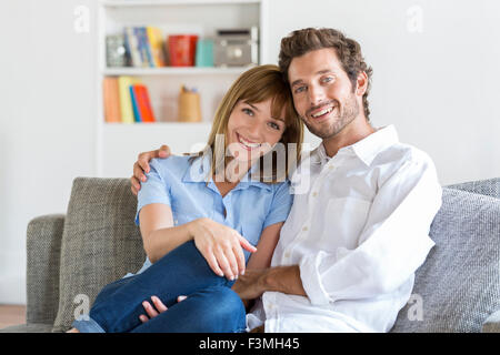 Portrait of cheerful trente ans couple sitting on sofa in modern appartement blanc Banque D'Images