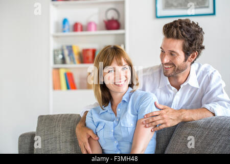 Portrait of cheerful trente ans couple sitting on sofa in modern appartement blanc Banque D'Images