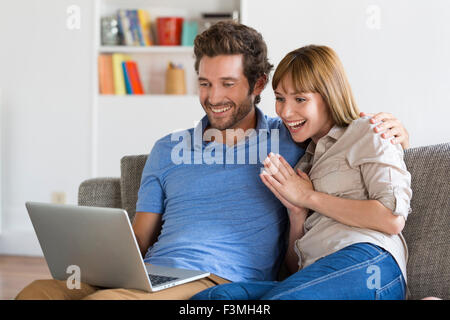 Heureux succès jeune couple avec ordinateur portable sur canapé blanc moderne en appartement. Banque D'Images