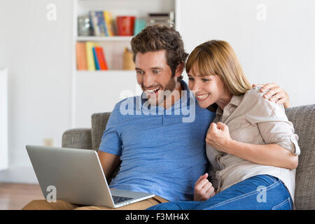 Jeune couple consulter les résultats de la loterie sur ordinateur portable blanc moderne dans la maison. Banque D'Images