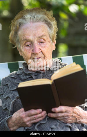 Une vieille femme lisant un livre assis dans un hamac. Banque D'Images