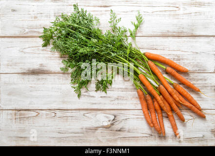 Les racines de carottes fraîches avec des feuilles vertes sur fond de bois. Concept d'aliments biologiques Banque D'Images