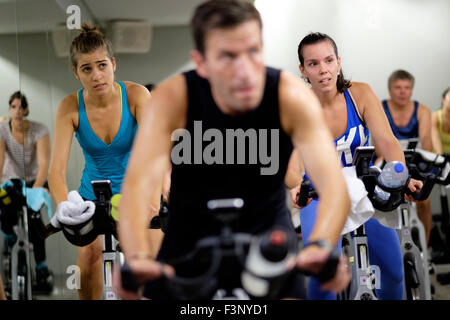 Les jeunes femmes équitation vélo stationnaire pendant un cours de gym spinning Banque D'Images