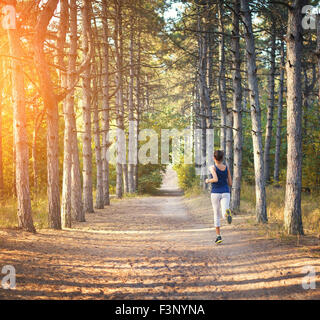 Jeune femme tournant sur un chemin rural au coucher du soleil dans la forêt d'automne. Fond sports Lifestyle Banque D'Images