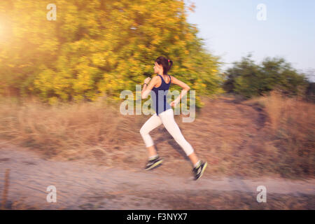 Jeune femme tournant sur un chemin rural au coucher du soleil dans la forêt d'automne. Fond sports Lifestyle Banque D'Images