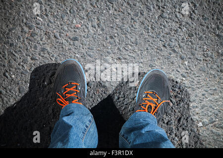 Pieds dans les chaussures de sport hommes debout sur la chaussée de la route d'asphalte Banque D'Images