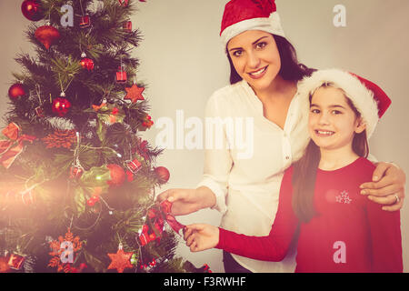 Mère et fille hanging Christmas decorations on tree Banque D'Images