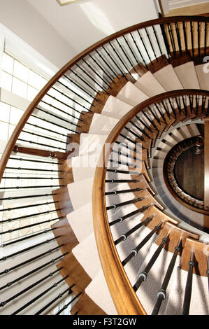 Un magnifique escalier ronde dans une photo gros plan sur trois étages en bois de chêne avec moquette et d'une fenêtre sur la gauche. Banque D'Images