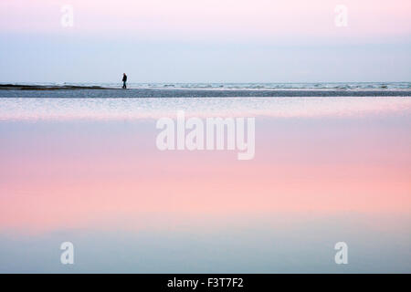 Lone man walking au crépuscule avec des réflexions sur la plage à Bexhill on Sea, East Sussex, England, UK Banque D'Images