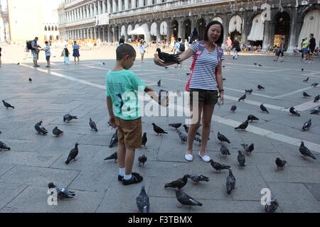 Une femme asiatique et un garçon jouer avec les pigeons à Venise Italie Banque D'Images