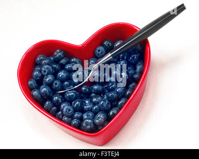 Les bleuets coeur coeur d'aliments santé concept / Les bleuets dans un plat en forme de coeur rouge avec cuillère design contemporain sur fond blanc Banque D'Images