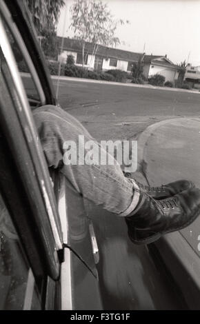 Un punk punk rocker portant des bottes de combat doc marten balance ses jambes sortir d'une voiture tournant un coin dans une région suburbaine voisin accueil hood de porterville, California 1980 fashion adolescents teen Banque D'Images