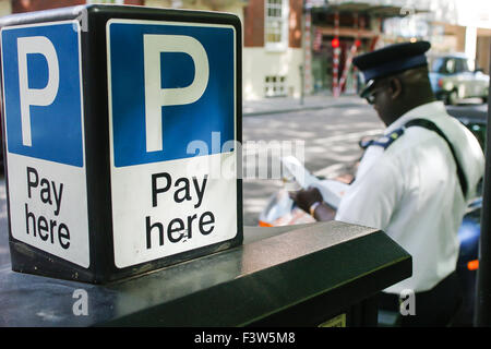 Un gardien de la circulation émet un ticket de stationnement pour une voiture stationnée illégalement alors qu'il se trouve près d'un guichet automatique de stationnement est montré à Westminster, Londres. Banque D'Images