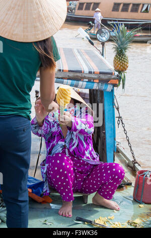 Jeune femme vietnamienne dame achète un ananas d'un vendeur au marché flottant de Cai Rang, Can Tho, delta du Mekong, Vietnam Banque D'Images