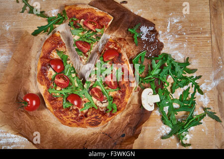 Délicieux, juteux et savoureux pizza végétarienne maison rustique sur planche de bois avec tomate cerise, roquette, mozzarella et basilic Banque D'Images