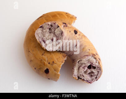 Un bagel bleuets fraîchement cassé en deux sur une planche de travail éclairé par la lumière naturelle. Banque D'Images