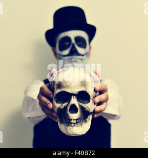 Un jeune homme avec le maquillage, le port de calaveras top hat, est titulaire d'un crâne effrayant en face de lui Banque D'Images