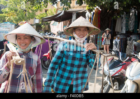 Hoi An, Vietnam. Deux femmes locales vente de fruits réalisées sur leurs jougs dans une scène de rue vietnamiens. Banque D'Images