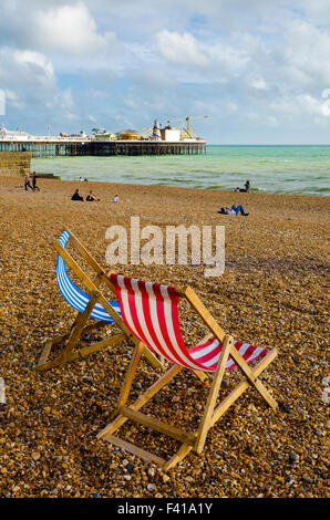 Deux chaises longues sur la plage de Brighton et Hove avec Brighton Pier dans la distance, East Sussex, Angleterre. Banque D'Images