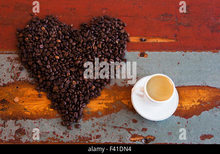 Forme de coeur de grains de café sur une table en bois vintage avec une tasse de café Banque D'Images