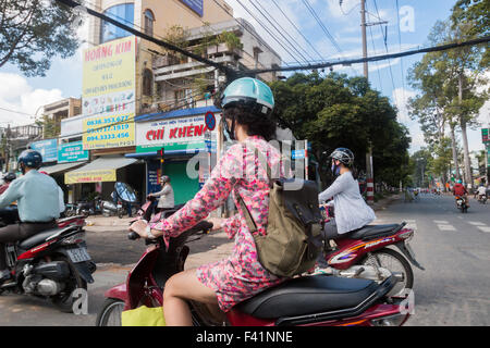 Dame vietnamienne et cavaliers masculins sur leurs scooters moto grâce à Ho Chi Minh ville ou Saigon, Vietnam centre Banque D'Images