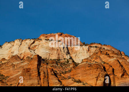 La belle lueur du soleil illuminant le grès rouge et orange rock formations contre un ciel bleu à Sion Nation Banque D'Images