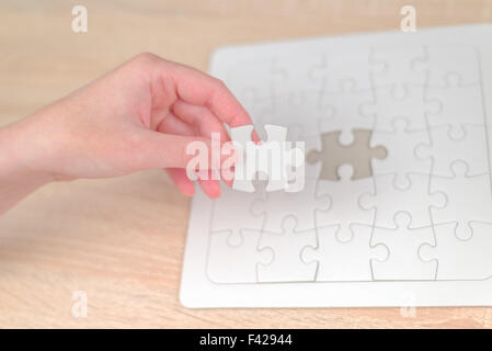 Mettre une main de femme pièce manquante et résoudre les casse-tête blanche placée sur le dessus de table en bois de chêne, Close up Banque D'Images