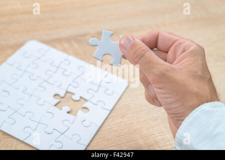 Businessman hand mettant une pièce manquante et résoudre les casse-tête blanche placée sur le dessus de table en bois de chêne, Close up, Banque D'Images