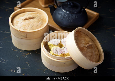 Dimsum situé dans le récipient en bambou avec théière sur fond noir Banque D'Images