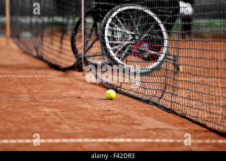 Joueur de tennis en fauteuil roulant non focalisé est vu derrière un filet de tennis sur une cour d'argile Banque D'Images