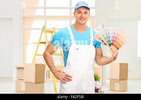 Jeune homme peintre dans une robe blanche tenant un échantillon de couleur dans un appartement et regardant la caméra Banque D'Images