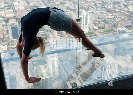 Woman doing backbend dans overservation à fond de verre pont à Willis Tower, Chicago, Illinois, États-Unis Banque D'Images