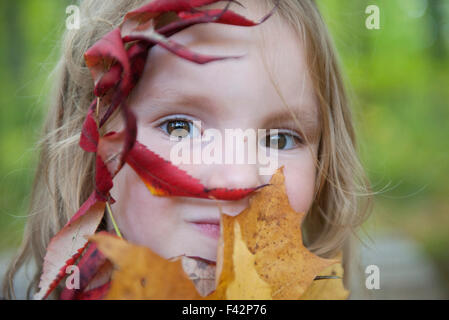 Girl holding autumn leaves devant sa face, portrait Banque D'Images