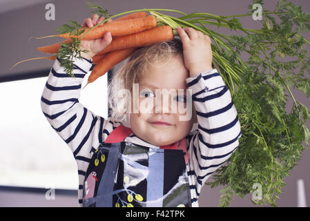 Little girl holding carottes fraîches sur sa tête, portrait Banque D'Images