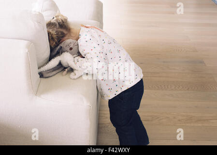 Petite fille cachant son visage dans les coussins canapé Banque D'Images