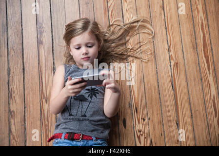 Little girl lying on floor using smartphone Banque D'Images