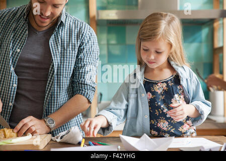 Petite fille dessin dans cuisine pendant que le repas se prépare en famille Banque D'Images