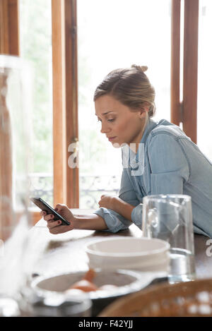 Young woman using smartphone in kitchen Banque D'Images