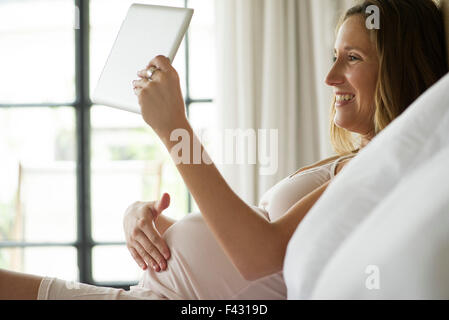 Pregnant woman using digital tablet de chatter en vidéo avec vos amis et votre famille Banque D'Images
