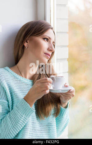 Belle jeune femme de race blanche de boire son café à l'appui de fenêtre. Rêve magnifique fille avec tasse de café Banque D'Images