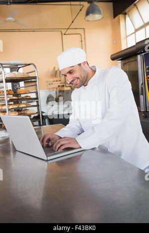 Smiling Baker à l'aide de l'ordinateur portable sur le plan de travail Banque D'Images