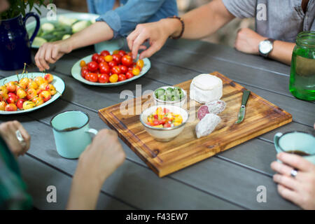 Un groupe de gens réunis autour d'une table avec des assiettes de fruits et légumes frais, et d'un fromage rond et le salami sur un Banque D'Images