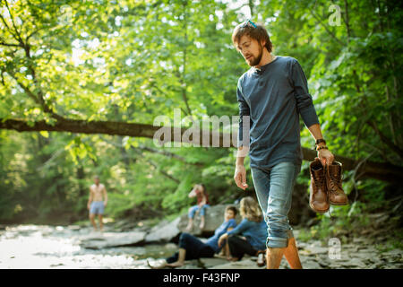 Un homme portant ses bottes marche sur les rochers par une rivière. Banque D'Images