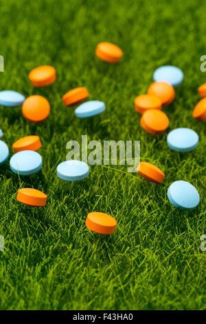 Orange et bleu dispersés comprimés ronds sur l'herbe verte.composition verticale Banque D'Images