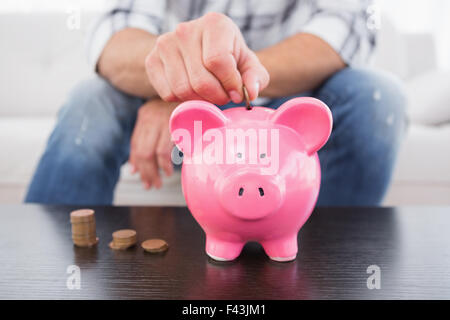 Un homme putting coins in piggy bank Banque D'Images