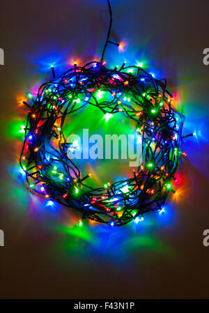 Une couronne de Noël multicolore créé par un ensemble de lumières câblé disposés dans un schéma circulaire en faible lumière pour des couleurs éclatantes. Banque D'Images